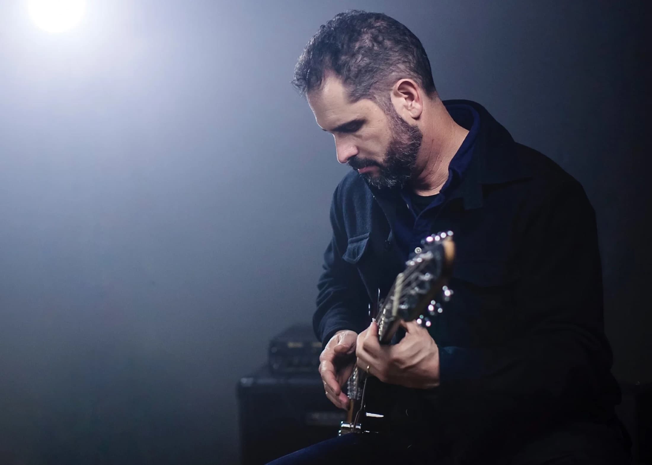 Charlie Hunter playing guitar under a single spotlight